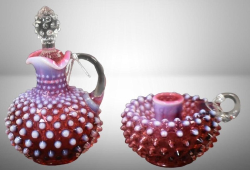 (2) Fenton Hobnail cranberry opalescent pcs: 7"h cruet w/ clear Hobnail stopper; 3"h finger hold candleholder